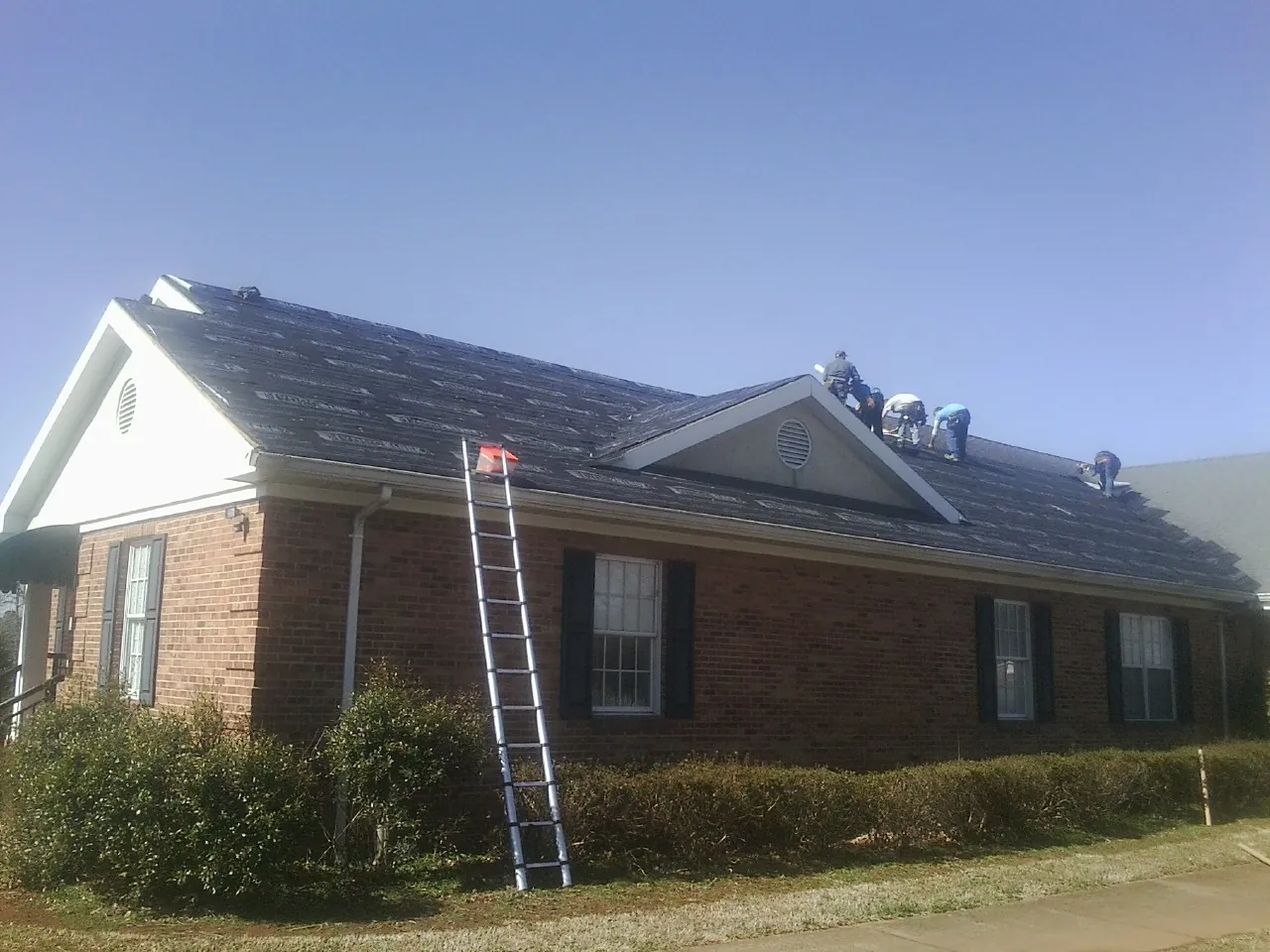 Crew tearing shingles off a brick ranch roof with a ladder set — Emergency Roof Repair work by our crew in Marlborough