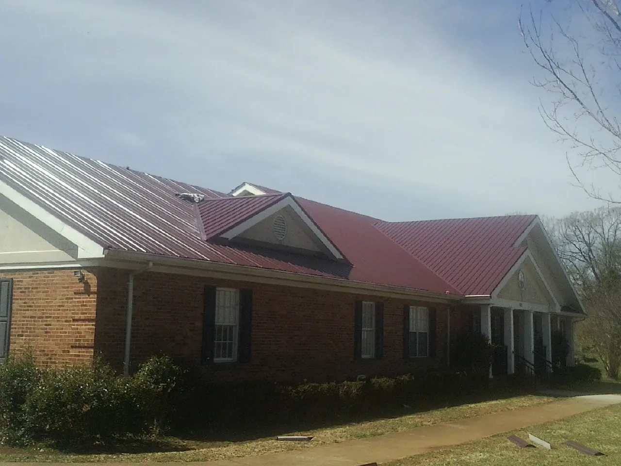 Red metal roof with gabled entries on a long brick building, from a Hail Damage Roof Repair job in Marlborough