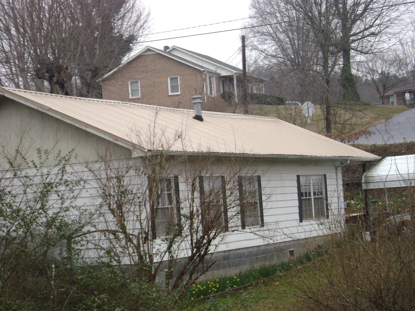 Tan metal roof on a white sided house set into a hillside — Commercial Roofing by Roofing Brothers in Marlborough